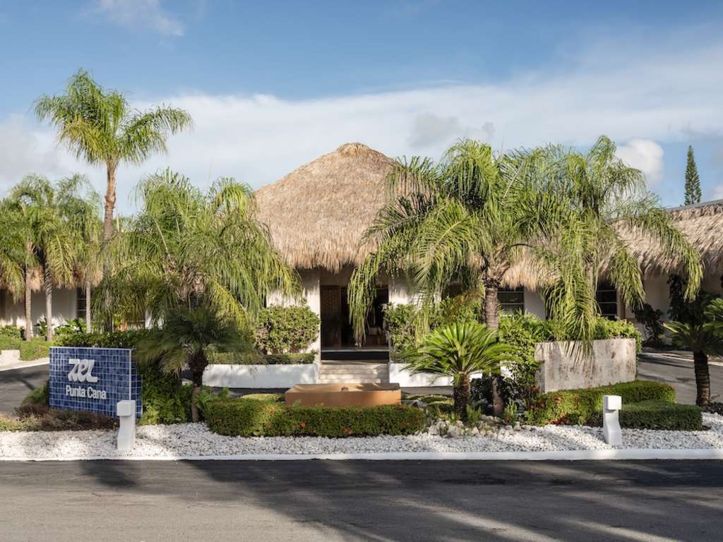 Exterior of Zel, a white building with a thatched roof surrounded by palm trees.
